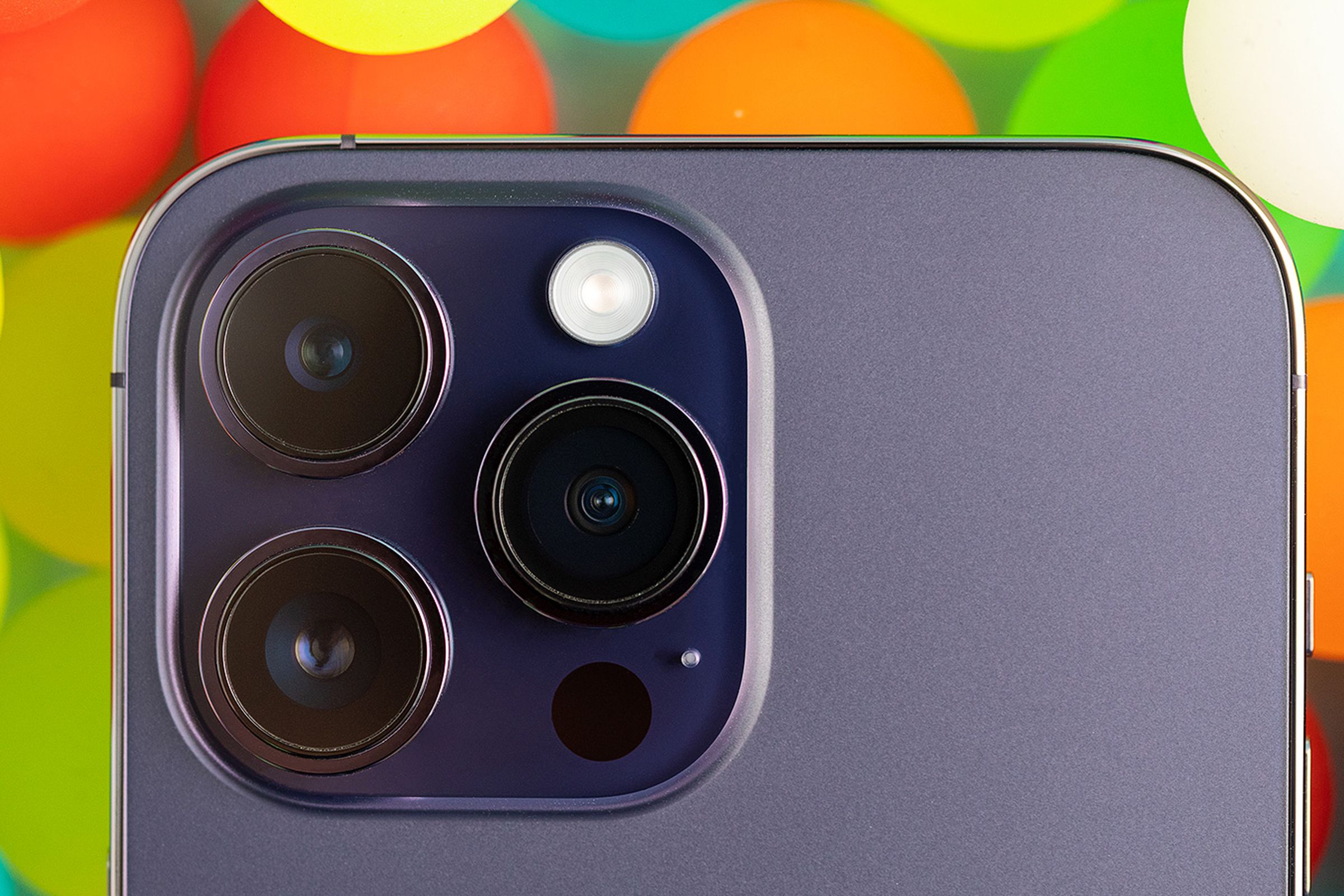 A close-up of the iPhone 14 Pro's camera module against a background of translucent colorful balls.